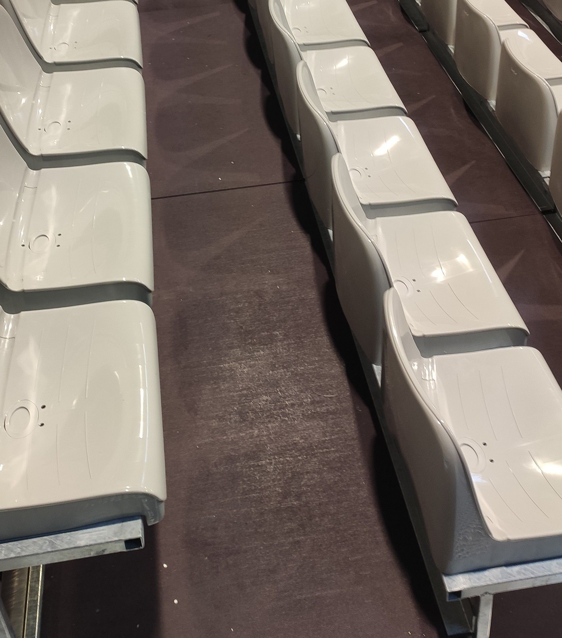 Reihen weißer, geschwungener Bänke mit dunkelgrauer Verzierung auf brauner Oberfläche.