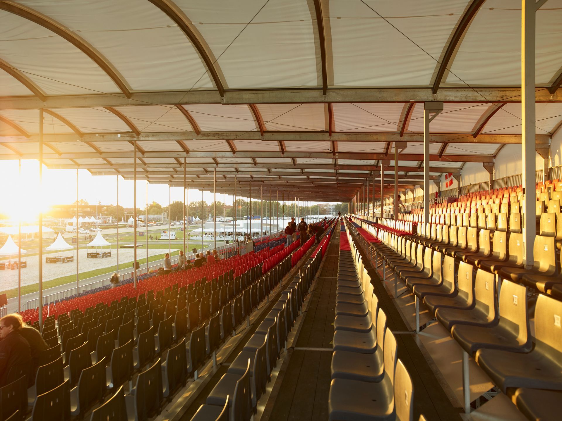 Reihen leerer Stadionsitze unter einem weißen Baldachin, in goldenes Sonnenlicht getaucht.