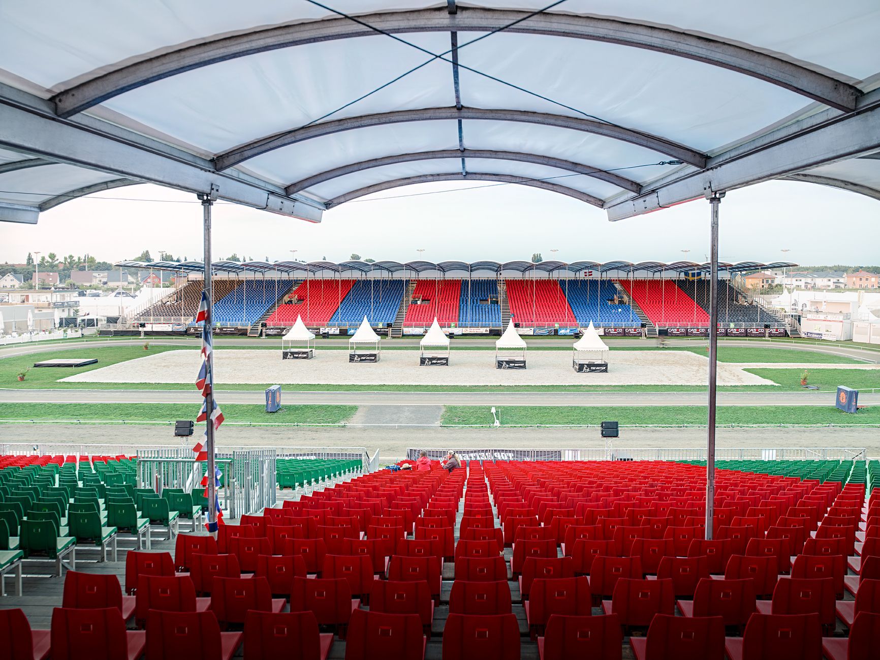 Stadionbestuhlung, roter und grüner Vordergrund, blaue und rote Tribünen im Hintergrund, unter einem weißen Baldachin.