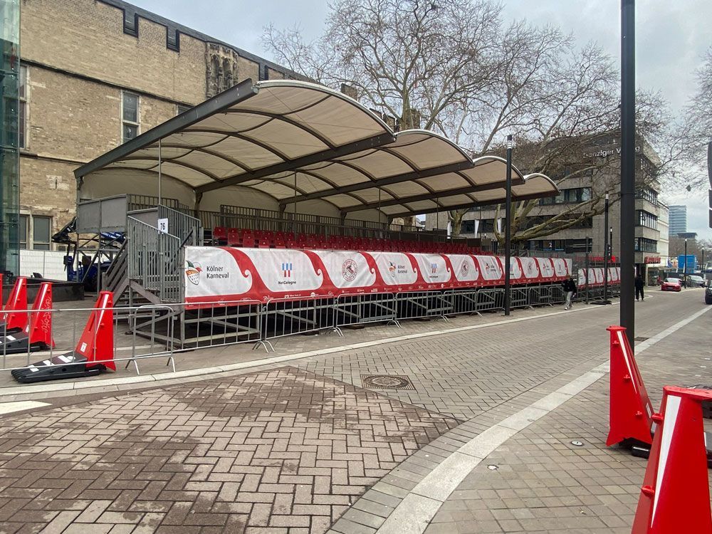 Outdoor covered platform stage set up on a city street, banners with logos, orange traffic cones.