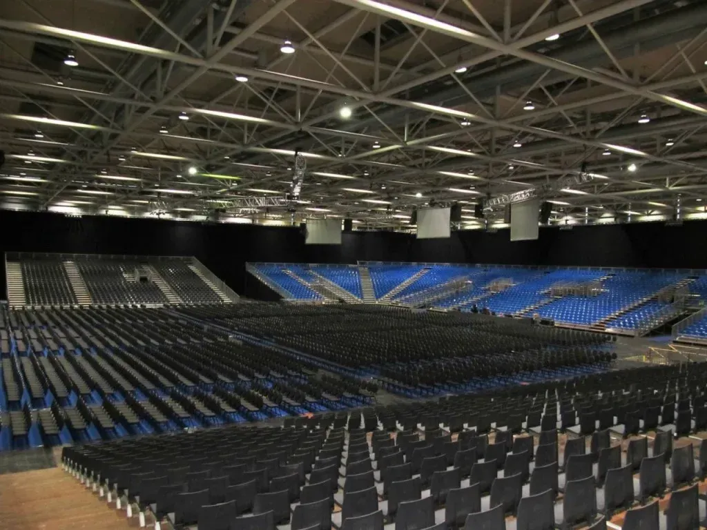 Leere Arena mit Reihen schwarzer und blauer Sitzplätze unter hellem Licht.