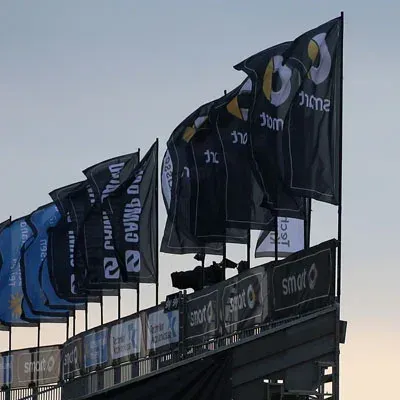 Fahnen mit dem Smart-Logo in Schwarzweiß auf einem Stadiongerüst vor bewölktem Himmel.