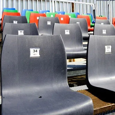 Reihen schwarzer Stadionsitze aus Kunststoff mit nummerierten Beschriftungen, einige mit farbigen Sitzen im Hintergrund.