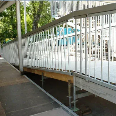 Rampe mit Metallgeländer; an einem sonnigen Tag sind die Stützen darunter sichtbar.
