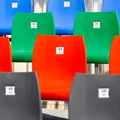 Bunte Stadionbestuhlung: blaue, grüne, rote und graue Stühle mit nummerierten weißen Etiketten.