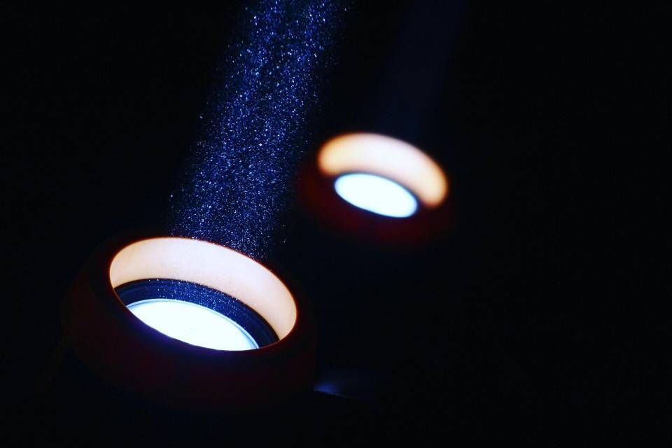 Zwei kreisförmige, leuchtende Ringlichter vor dunklem Hintergrund, wobei über dem näheren Ringlicht ein Lichtstrahl sichtbar ist.