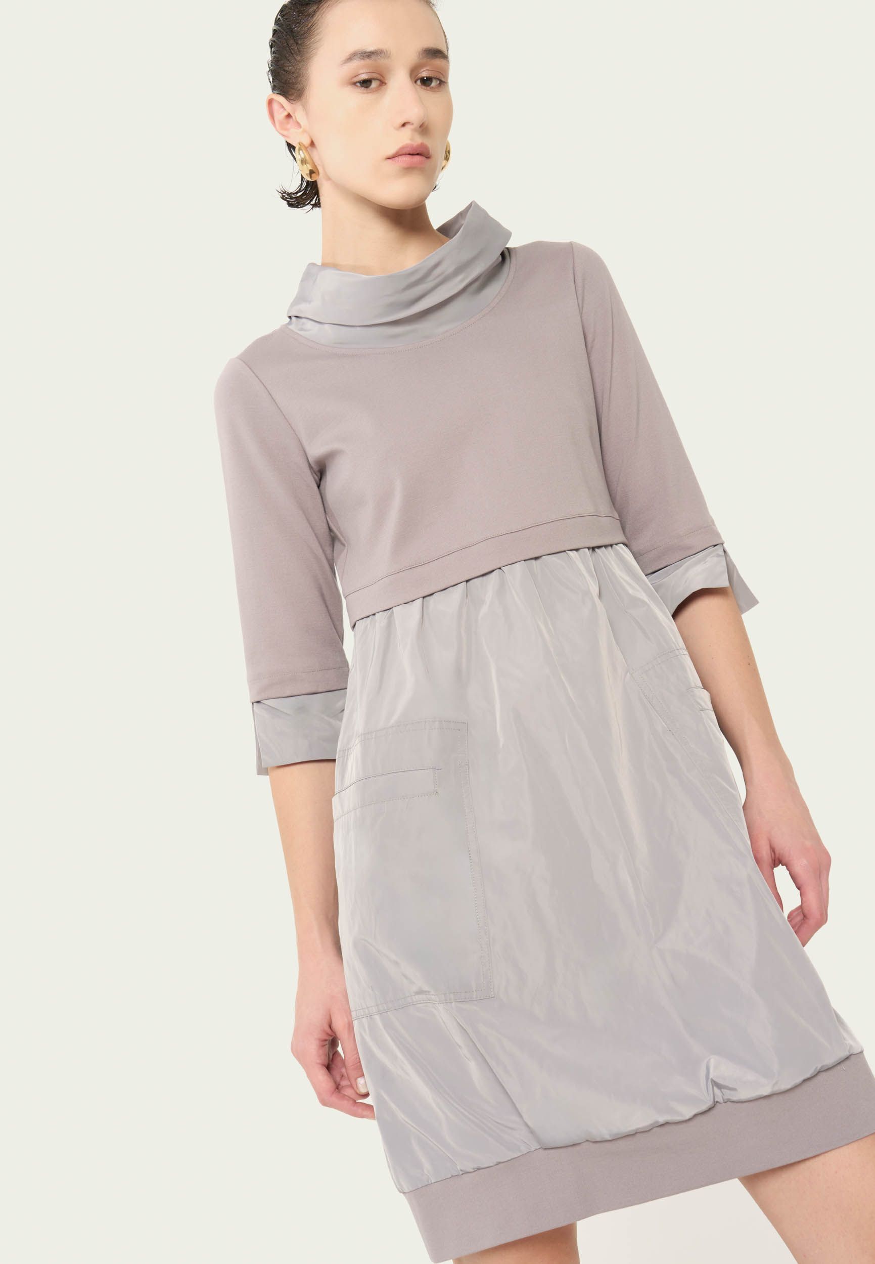 Eine Frau trägt ein graues Kleid mit Rollkragen.