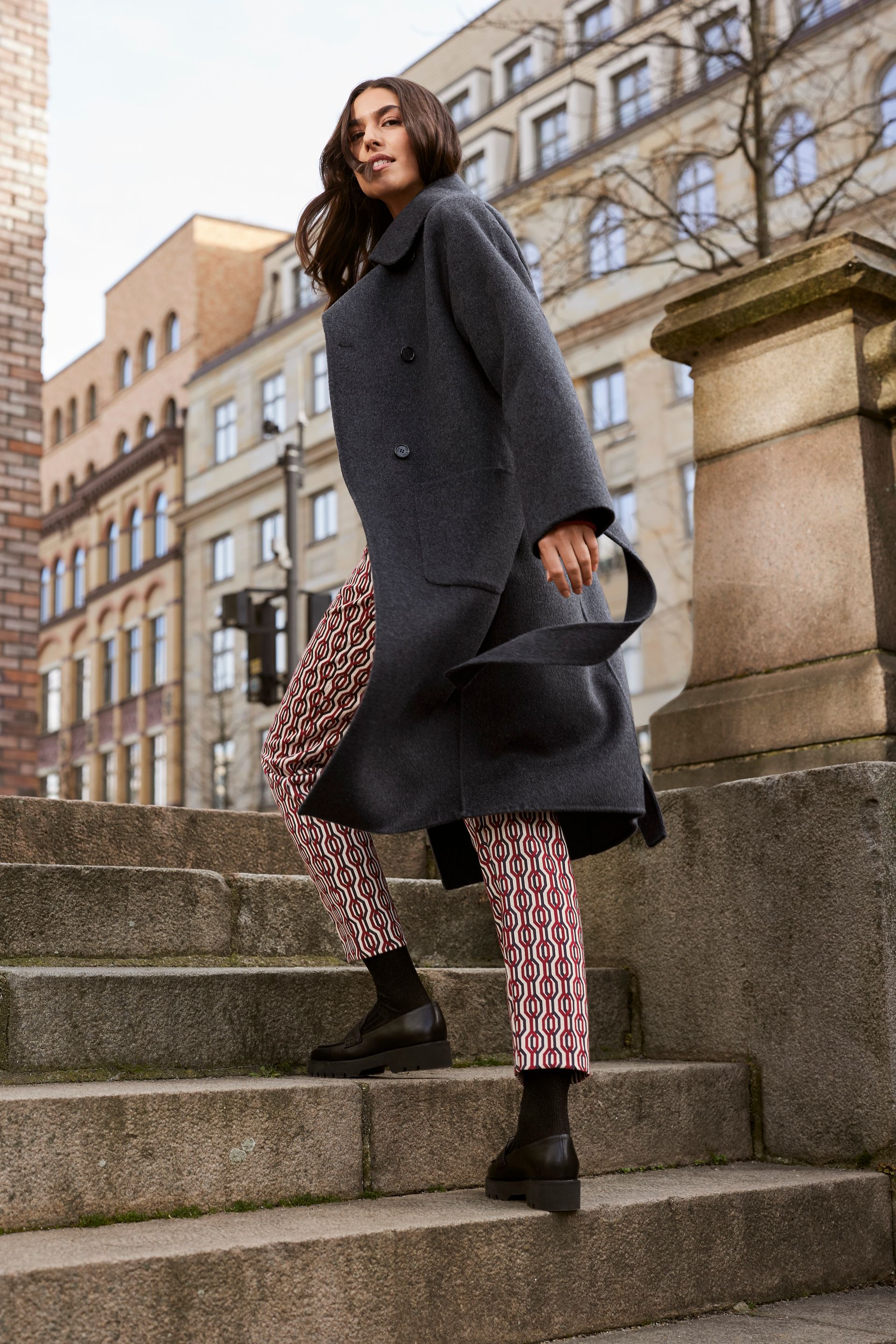 Eine Frau in einem grauen Mantel und Hosen mit Leopardenmuster steht auf einer Treppe.