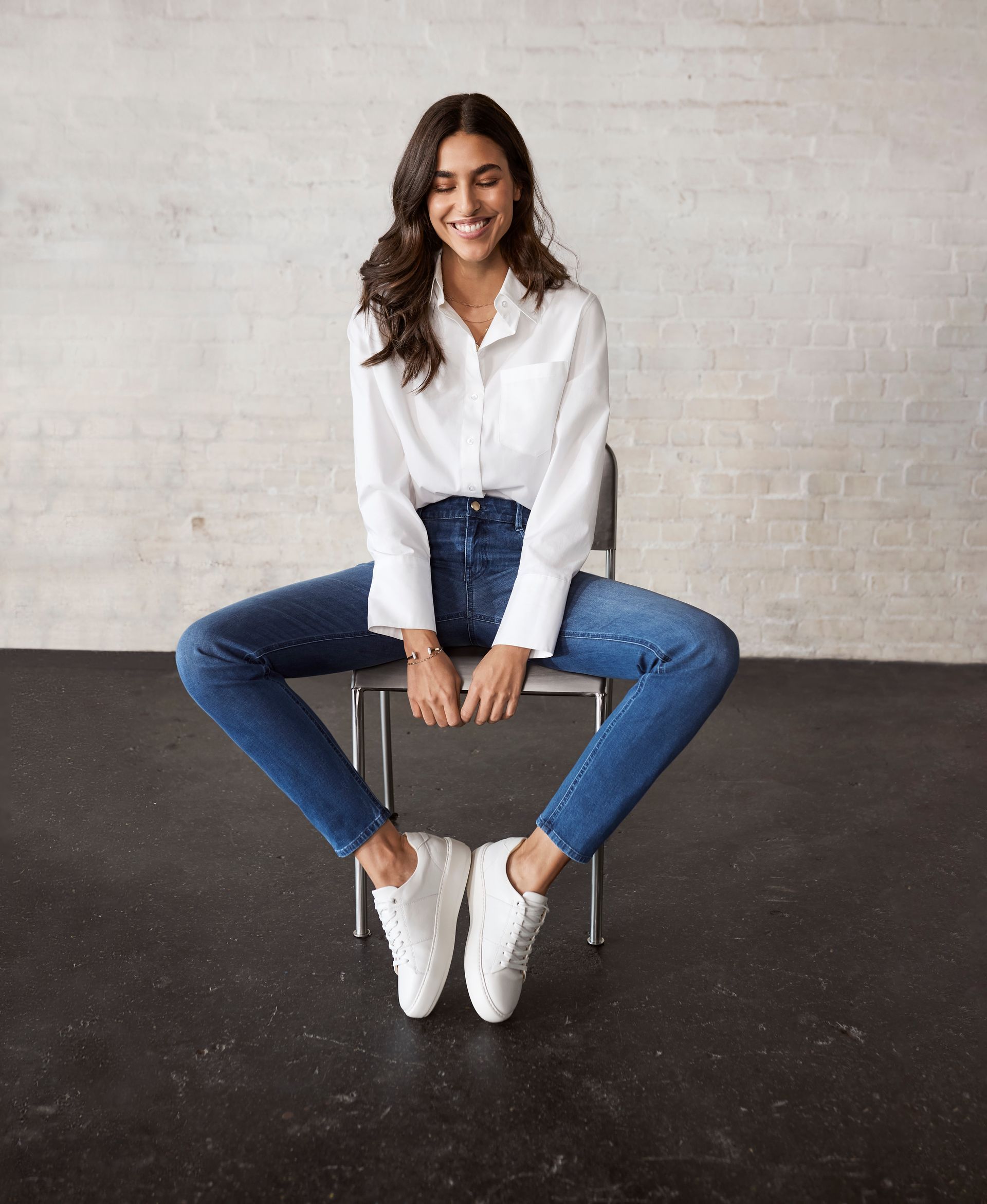 Eine Frau in einem weissen Hemd und blauen Jeans sitzt auf einem Stuhl.