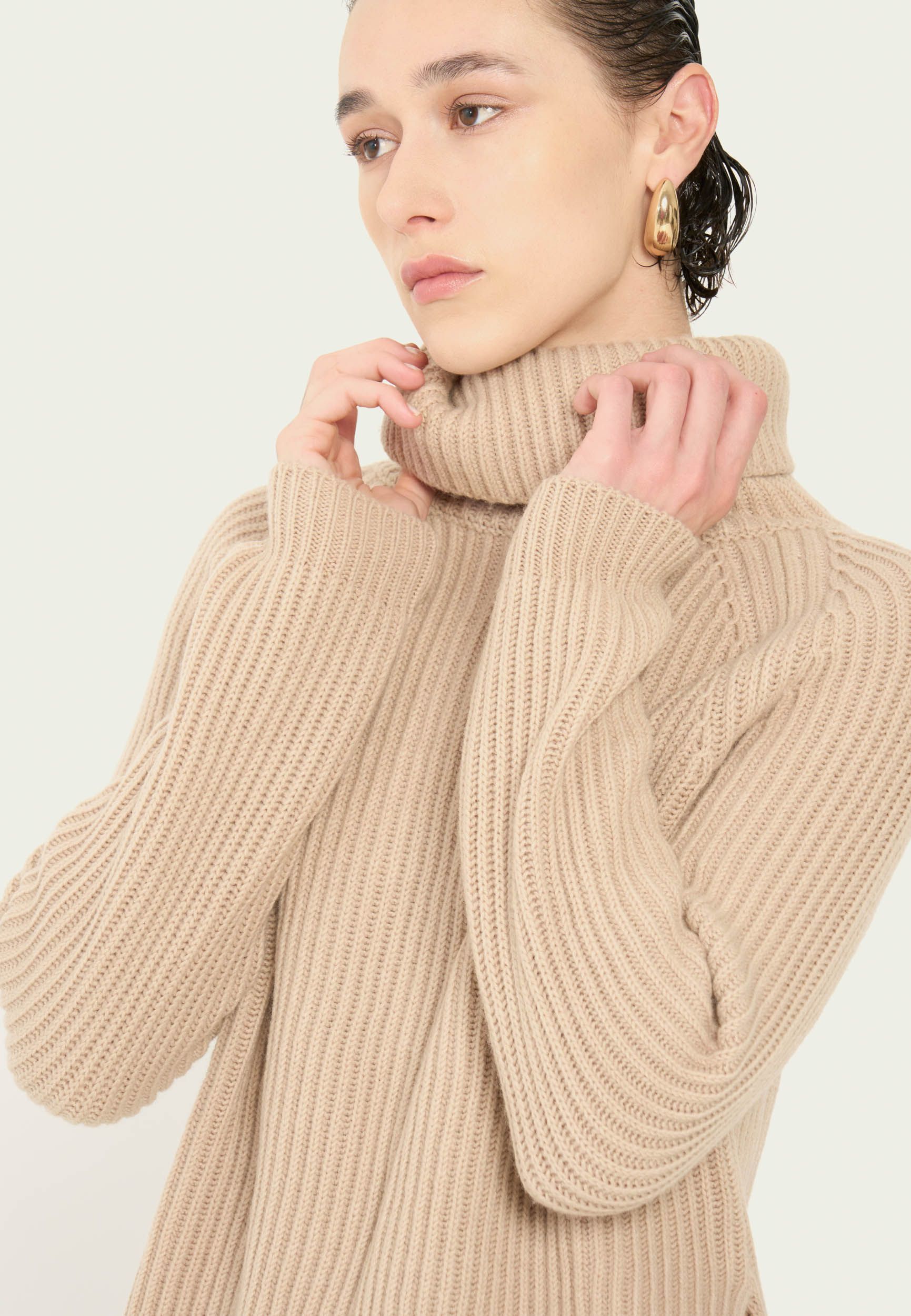 Eine Frau trägt einen hellbraunen Pullover mit Rollkragen.