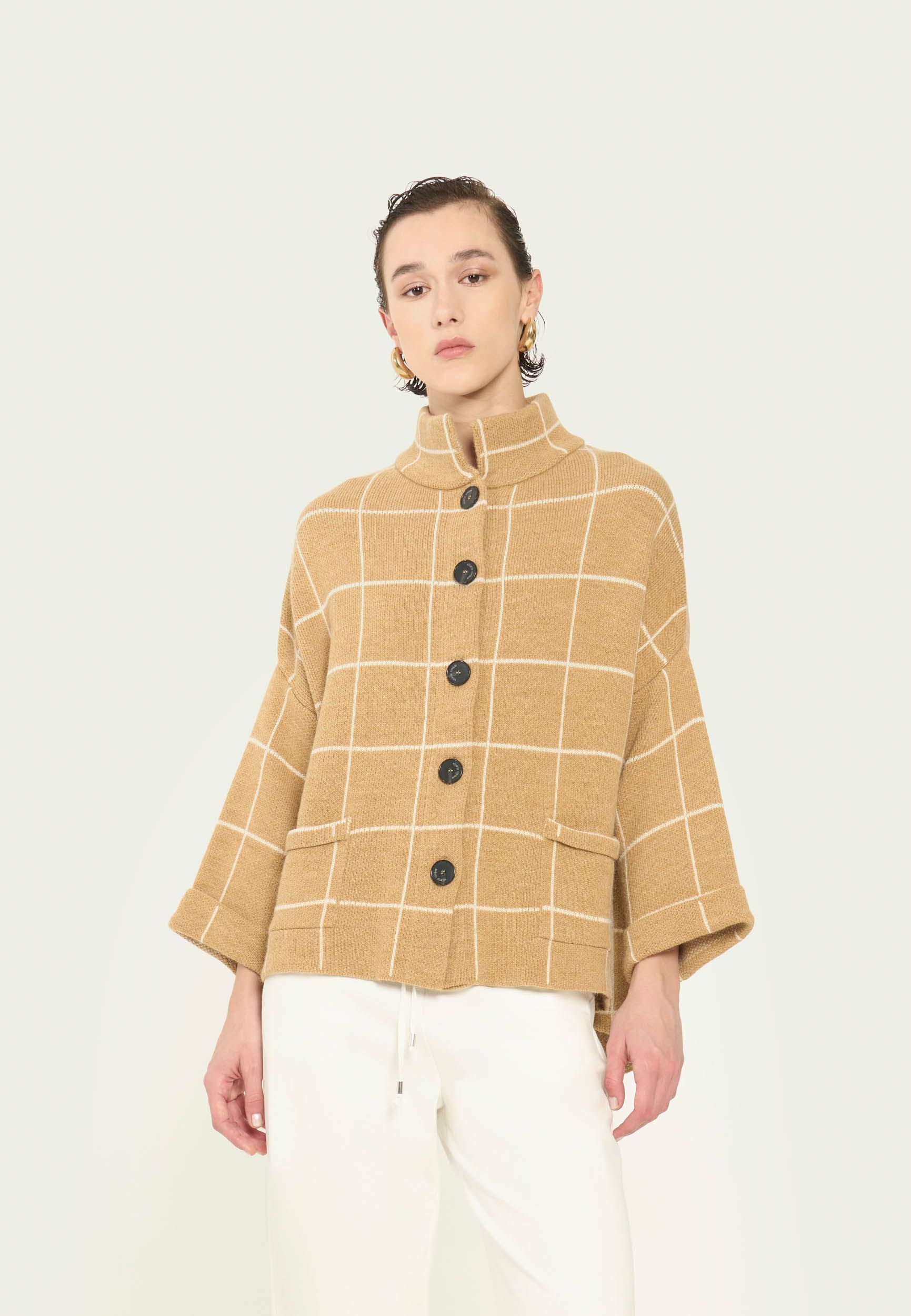 Eine Frau trägt eine karierte Jacke und eine weisse Hose.