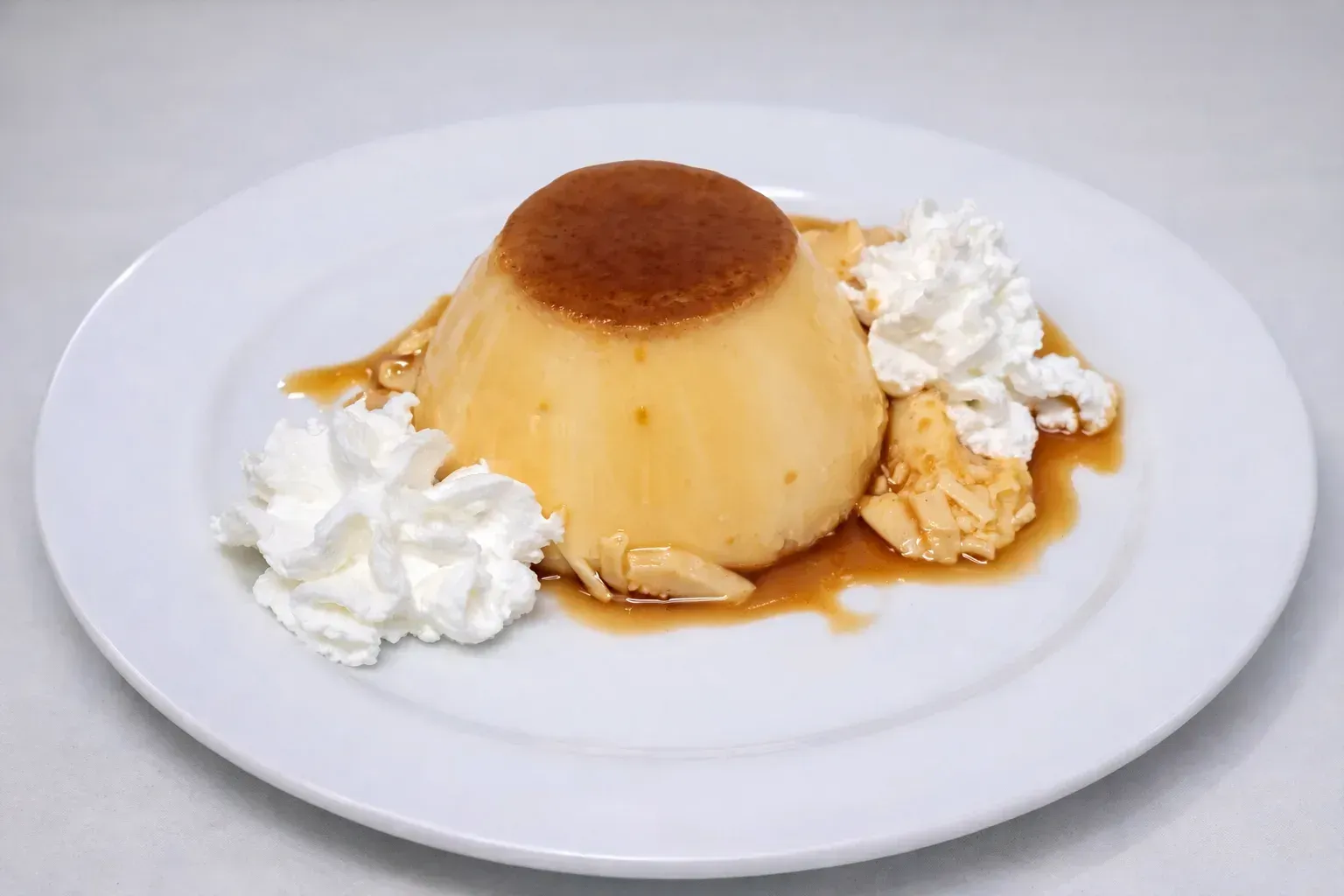 Postre de flan en plato blanco, rociado con caramelo y crema batida.