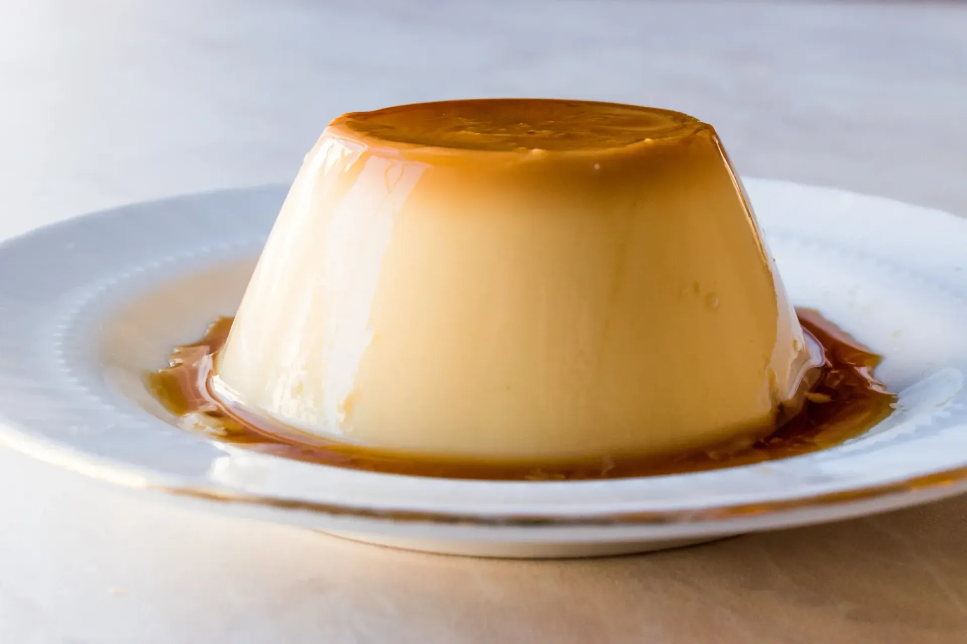 Postre de flan en plato blanco, salsa de caramelo rodeándolo.