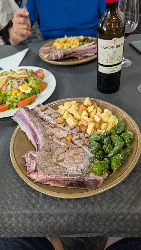 Plato de filete, patatas y pimientos con una botella de vino tinto y ensalada en una mesa.