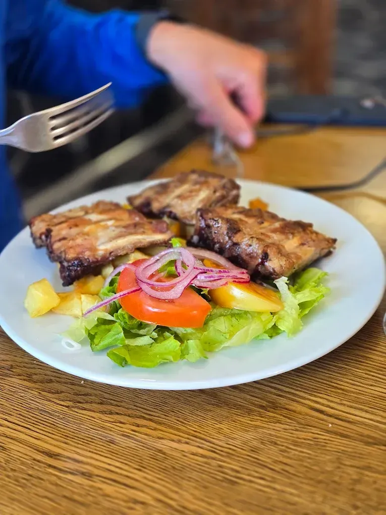 Plato de carne a la parrilla con ensalada y patatas fritas, que se come con tenedor.