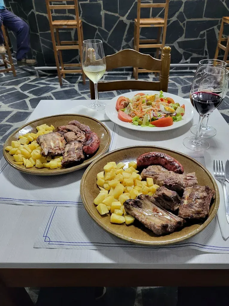 Dos platos de carne y patatas, ensalada, vino blanco y tinto en una mesa de un restaurante.