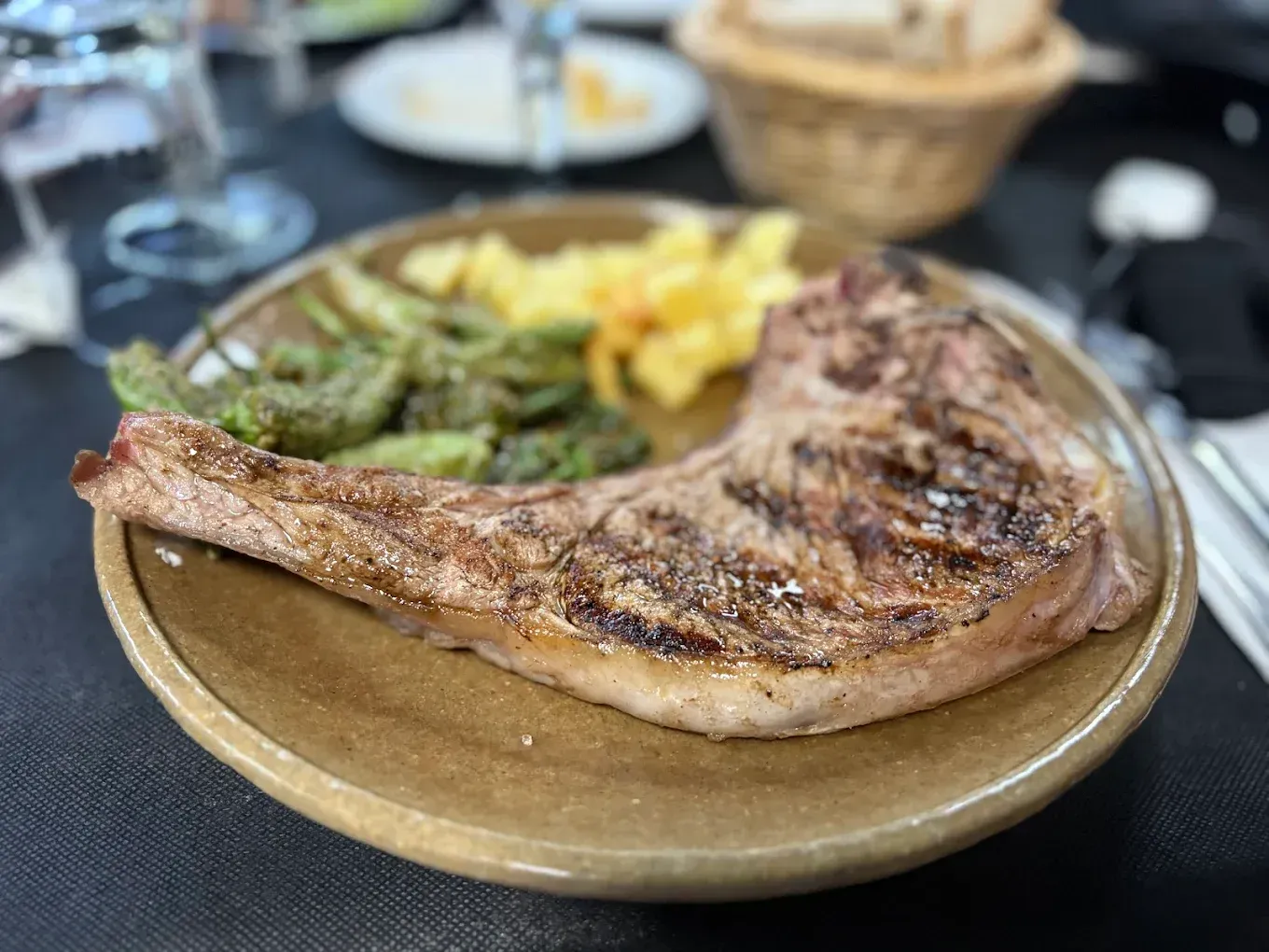 Bistec a la parrilla en un plato con pimientos verdes y patatas amarillas.