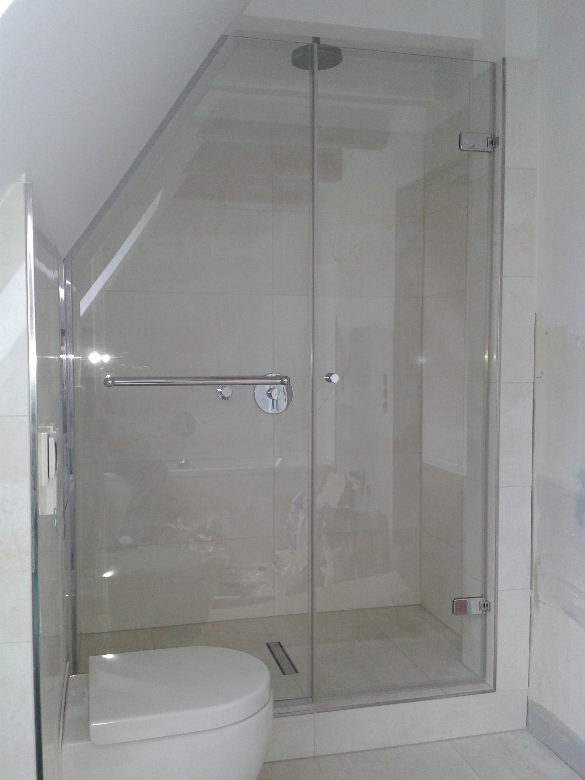 Kleines Badezimmer mit Duschkabine aus Glas und weißer Toilette unter einer Dachschräge.
