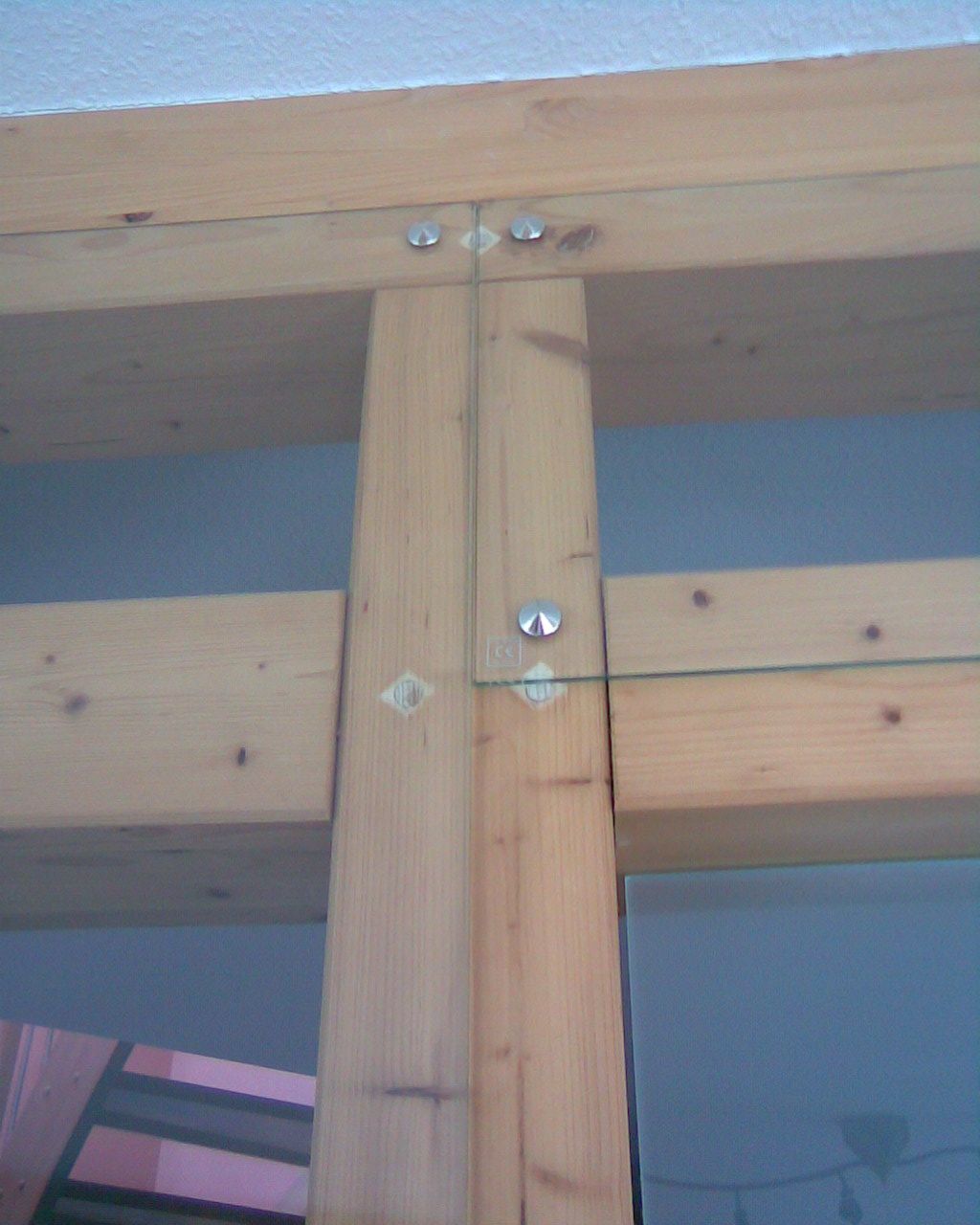 Nahaufnahme einer Holzbalkenverbindung mit Metallschrauben an einer blauen Wand.