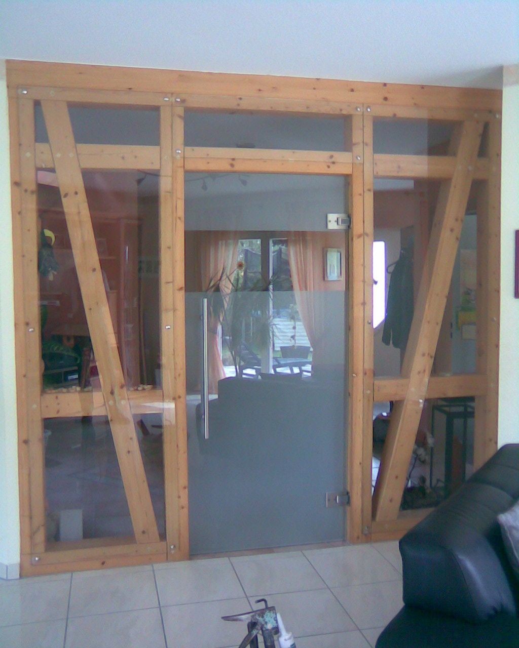 Großer, holzgerahmter Türbogen mit Glasscheiben, schrägen Stützen und einer zentralen Glastür in einem gefliesten Raum.