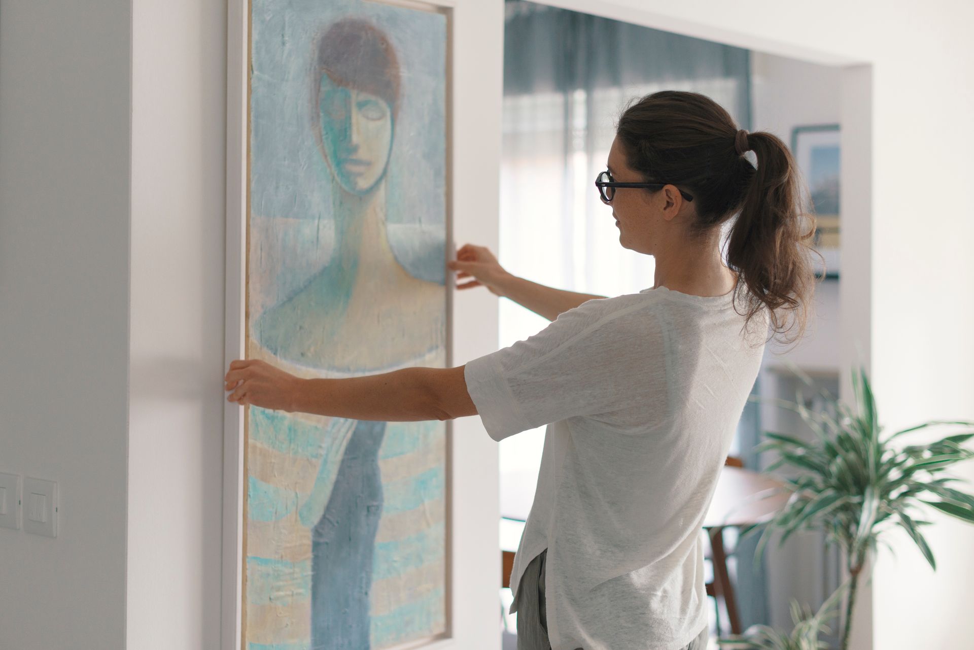 Une femme regarde et tient un tableau accroché au mur