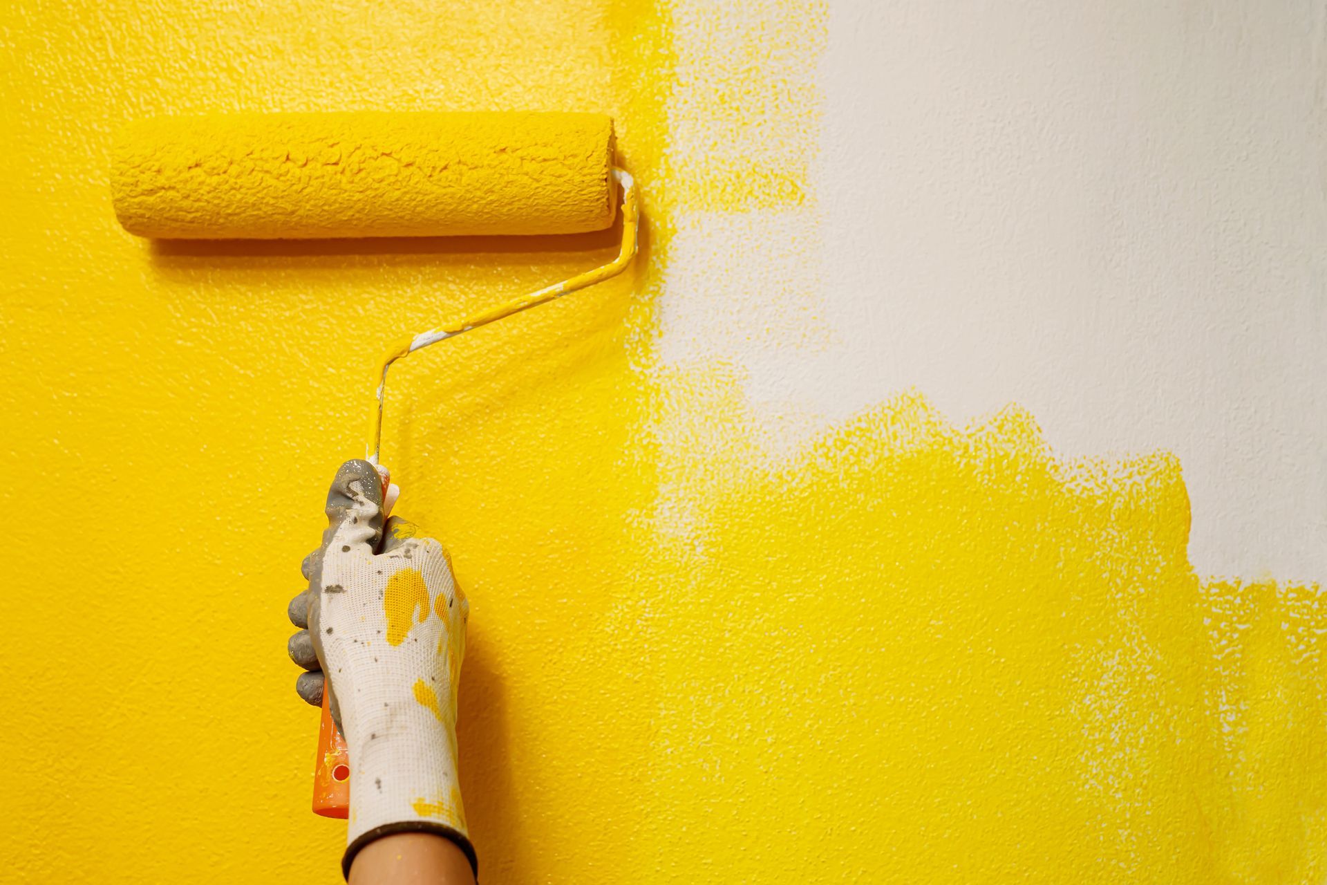 Main gantée de blanc : elle peignait un mur en jaune vif au rouleau.