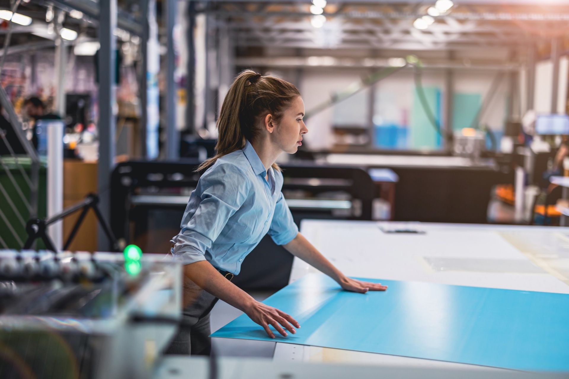 Mujer con camisa azul claro trabajando con una sábana azul grande sobre una mesa en un taller.
