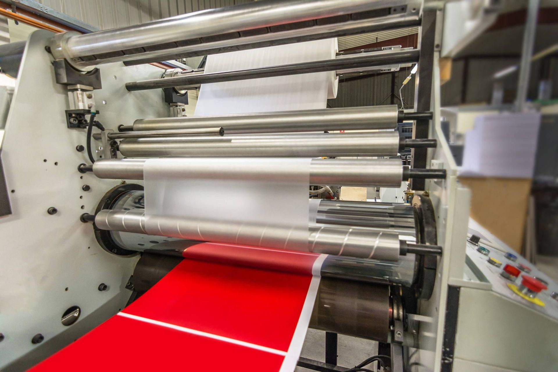 Máquina de impresión con material rojo y blanco en proceso de laminación.