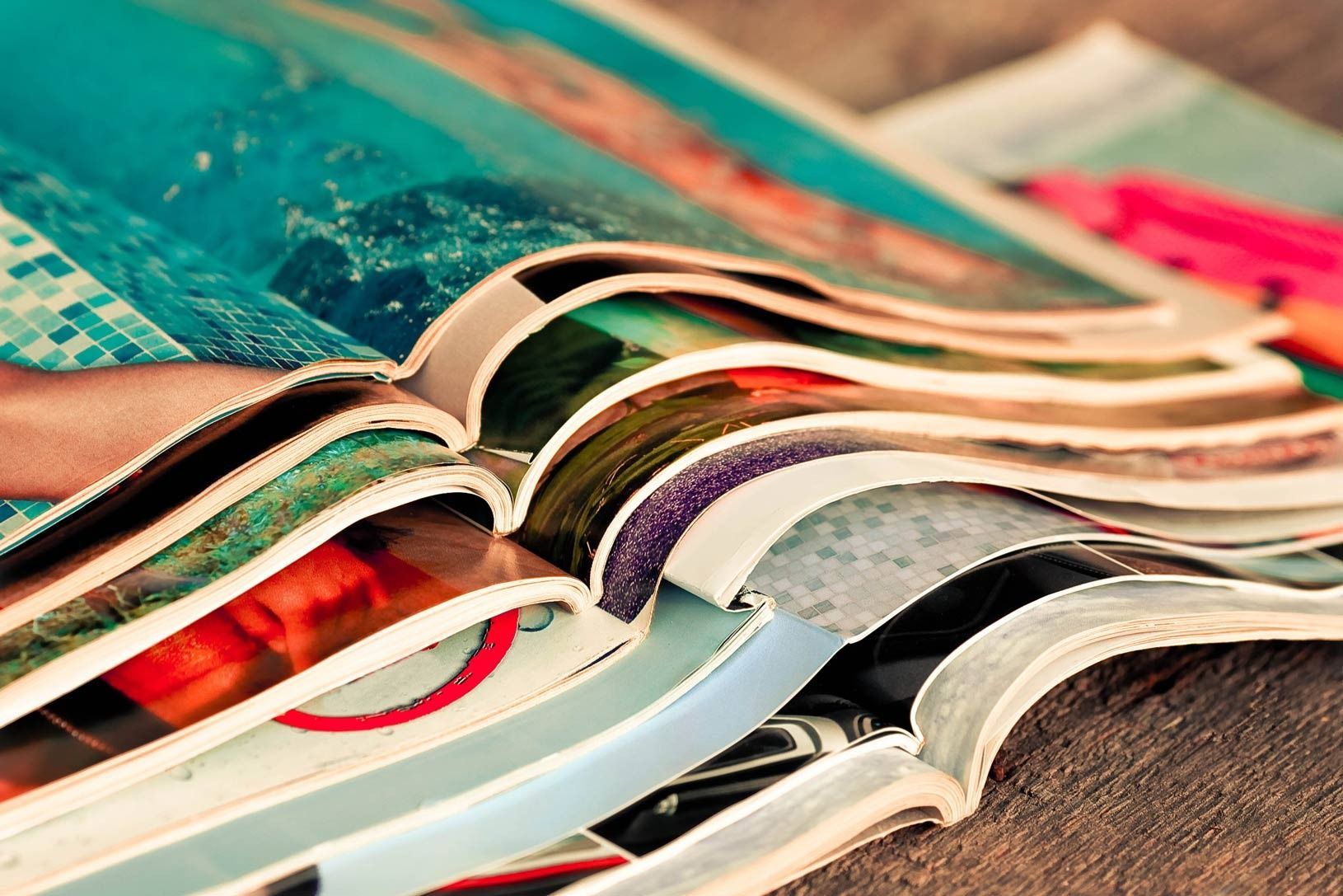Pila de revistas coloridas, abiertas con imágenes vibrantes, apiladas sobre una superficie de madera.
