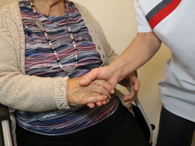 Mitarbeiterin hält Hand von Bewohner des Pflegezentrums GerAtrium