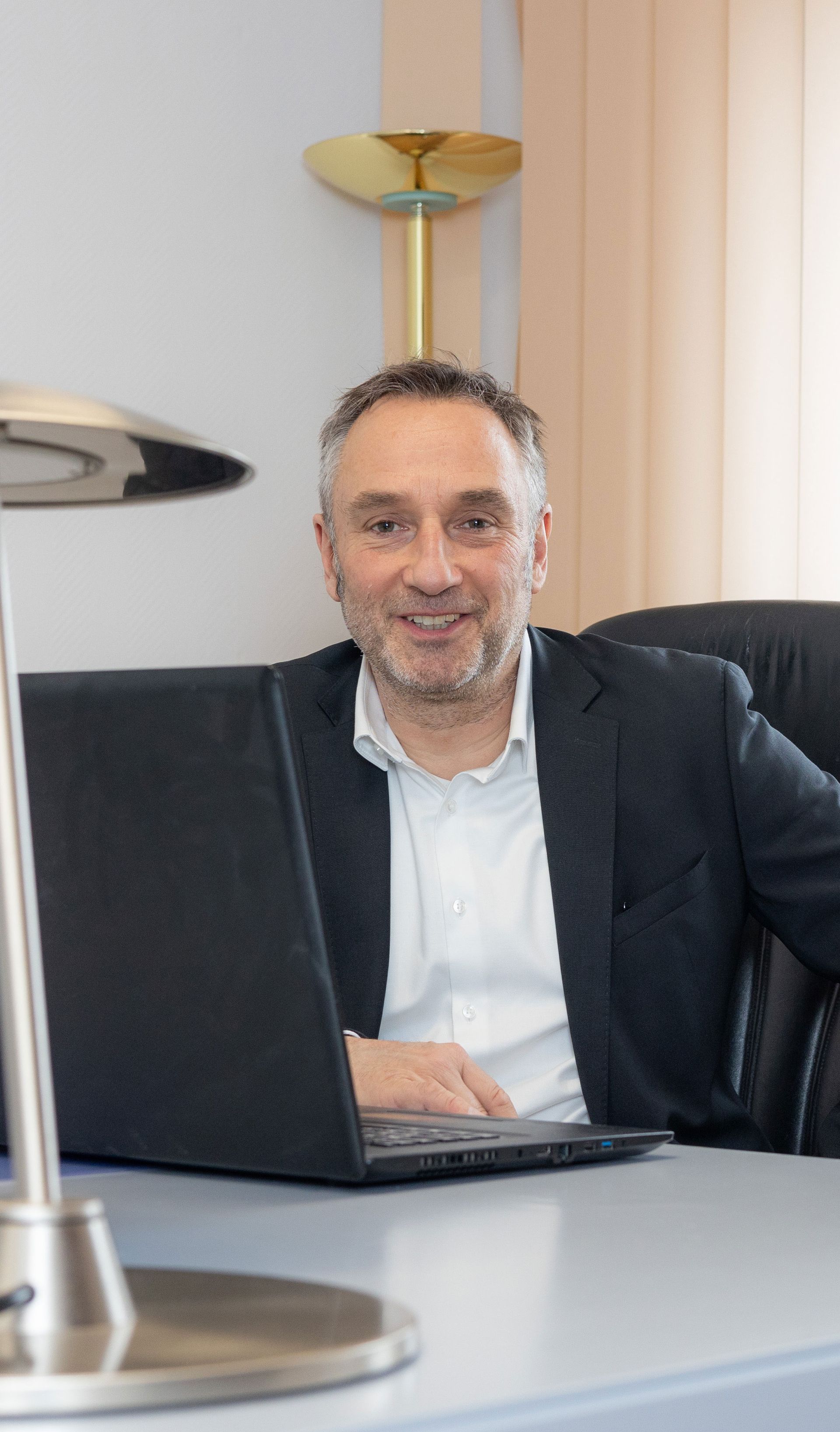 Ein Mann im Anzug sitzt mit einem Laptop an einem Schreibtisch.