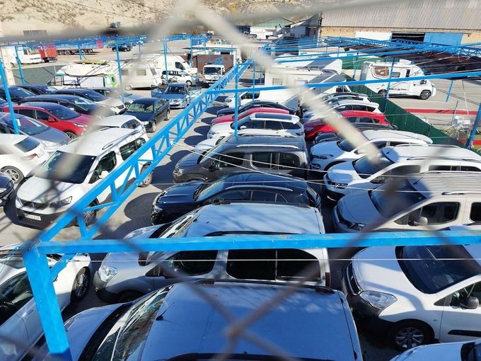 Hay muchos coches aparcados en un lote detrás de una valla de alambre.
