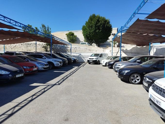 Hay muchos coches aparcados bajo sombrillas en un estacionamiento.