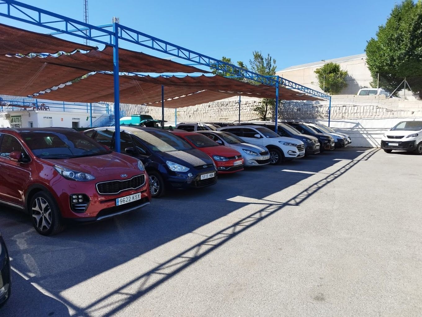 Una fila de coches están aparcados bajo un toldo en un estacionamiento.