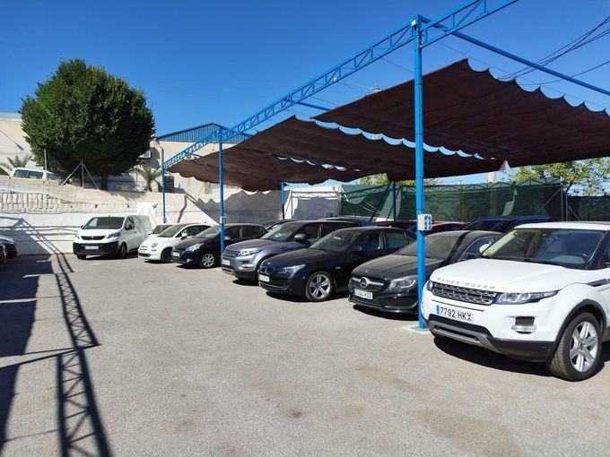 Una fila de coches están aparcados bajo un toldo en un estacionamiento.