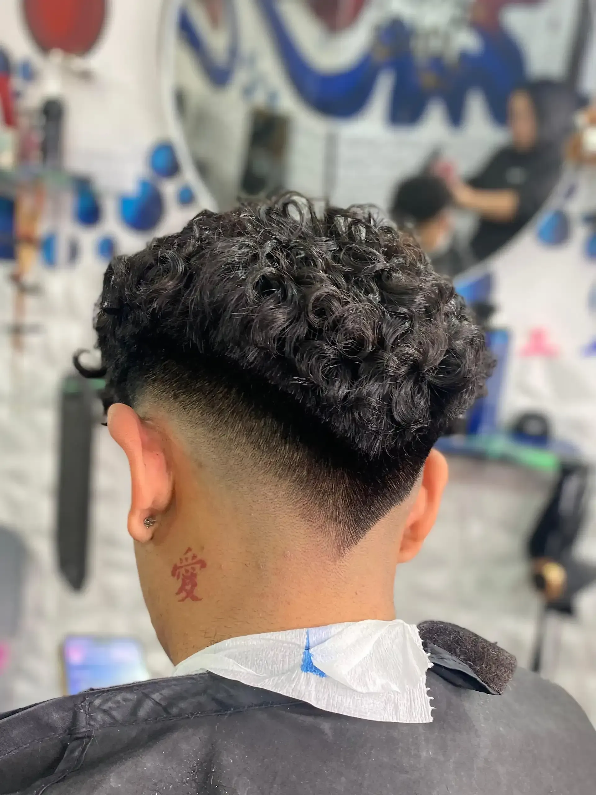 Una persona con cabello negro rizado y un corte de pelo descolorido en una barbería.