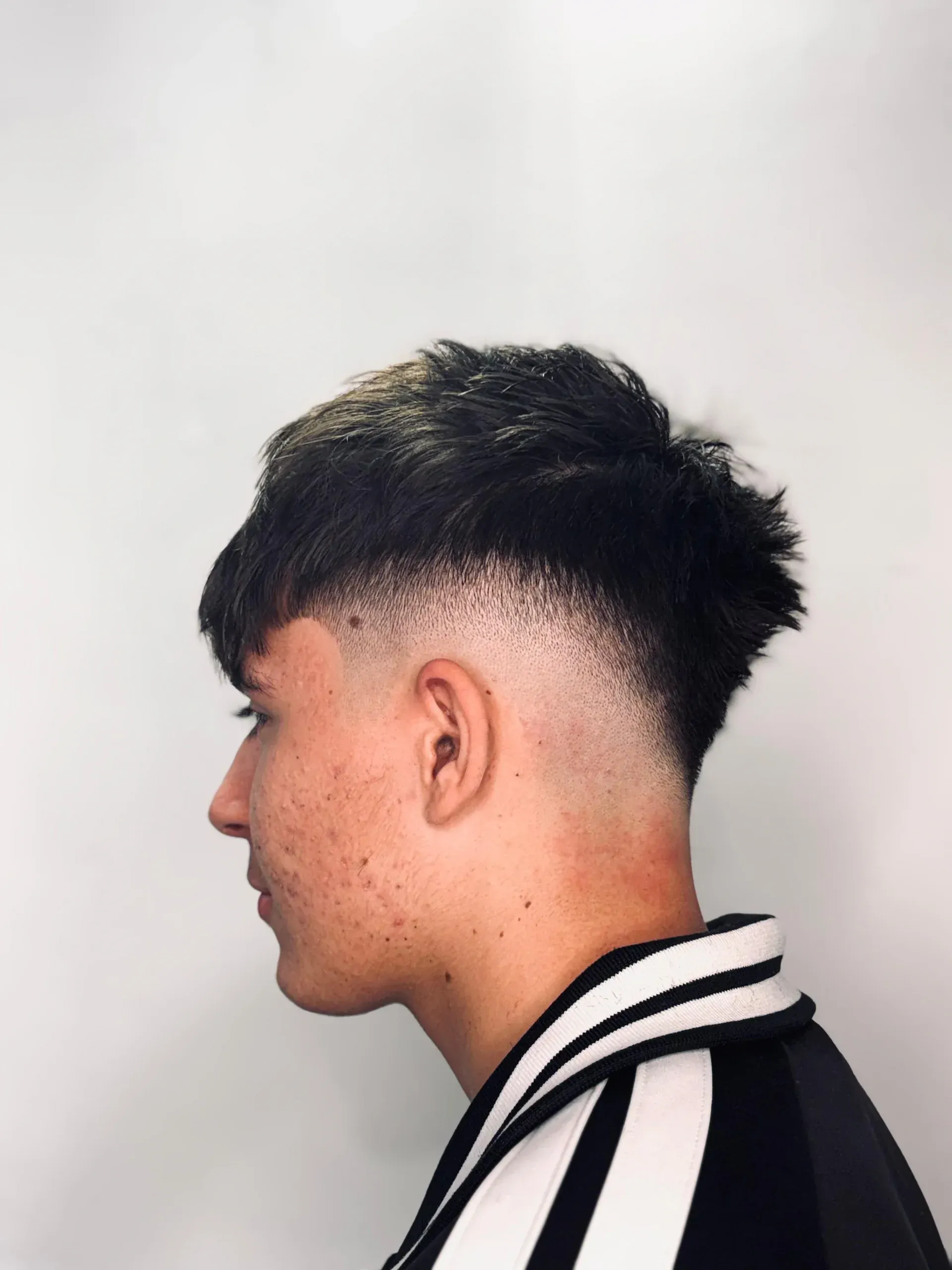 Persona joven con corte de pelo descolorido, cabello oscuro en la parte superior, perfil lateral.