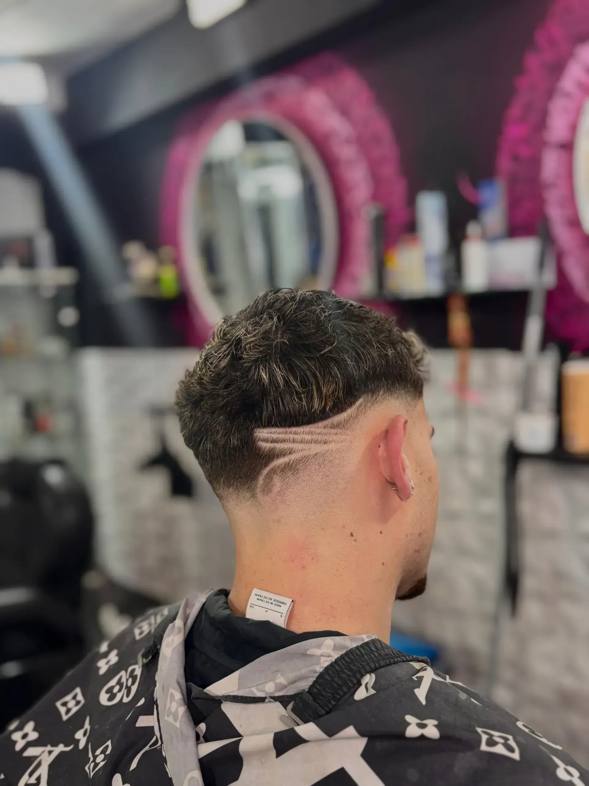 Hombre con corte de pelo desvanecido y diseño lateral. En una barbería con decoración rosa.