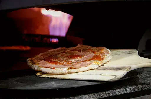 Se saca una pizza del horno sobre una pala de madera.
