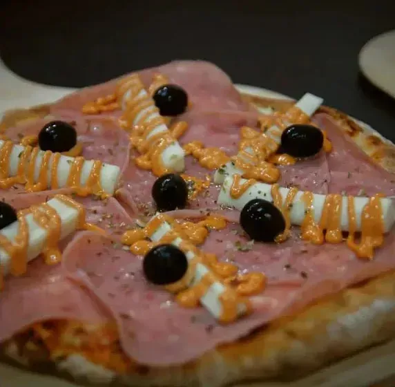 Una pizza con jamón, queso, aceitunas y salsa sobre una mesa.