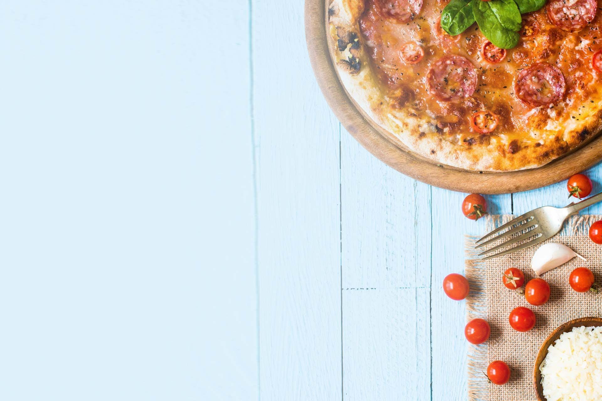 Una pizza en una tabla de cortar de madera con tomates y queso sobre una mesa de madera azul.