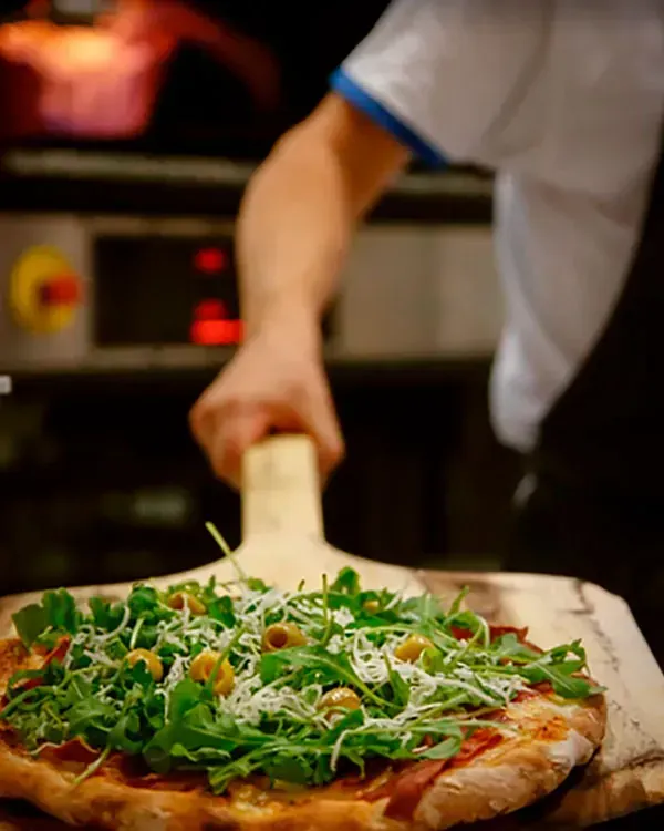 Una persona está poniendo una pizza en una paleta de madera.