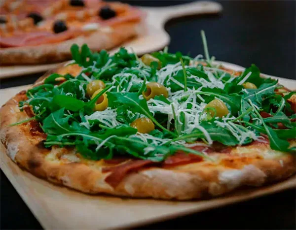 Una pizza con muchos ingredientes encima está sobre una tabla de cortar de madera.