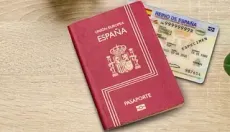 Un pasaporte español está sobre una mesa de madera al lado de un documento de identidad español.
