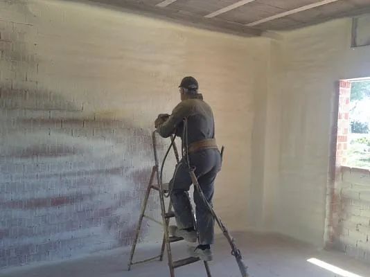 Un hombre está de pie en una escalera rociando espuma en una pared.