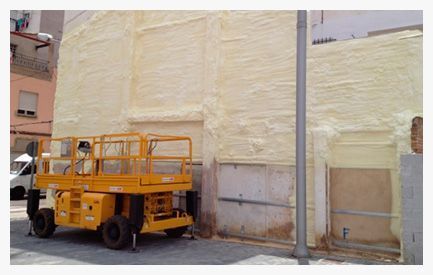 Un elevador de tijera amarillo está estacionado frente a un edificio cubierto de espuma.