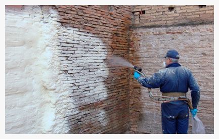 Un hombre está rociando espuma sobre una pared de ladrillos.