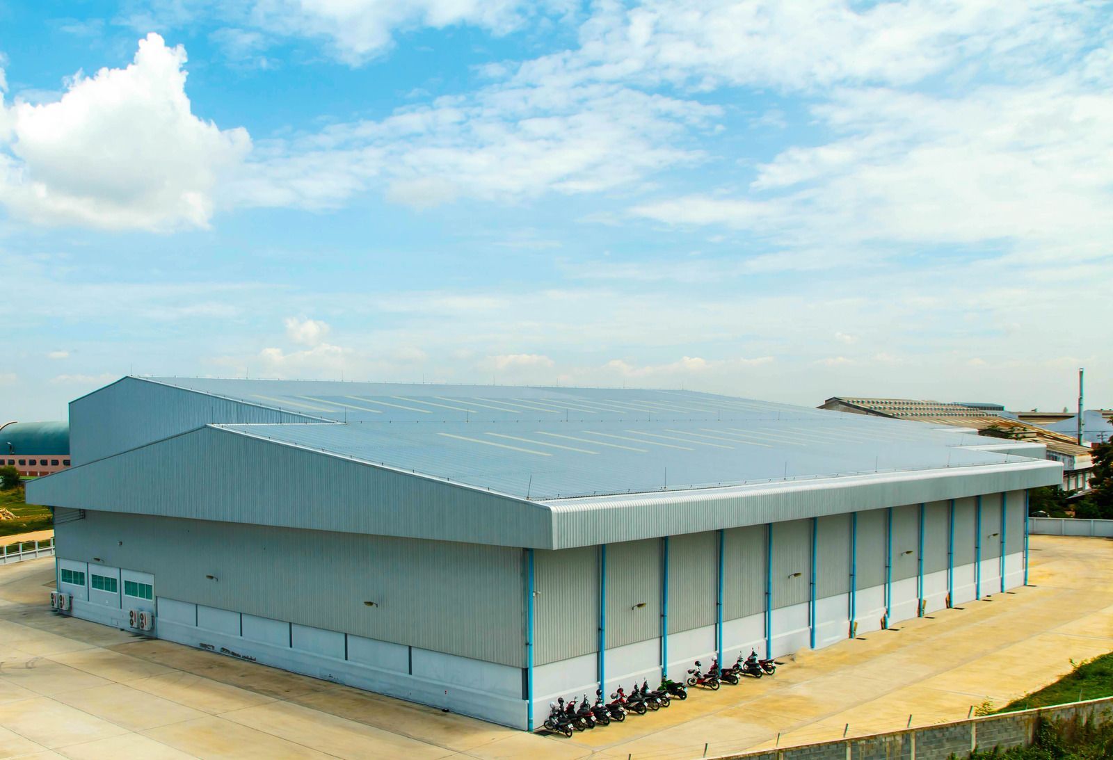 Large gray industrial warehouse with a sloped roof in an open lot under a blue sky