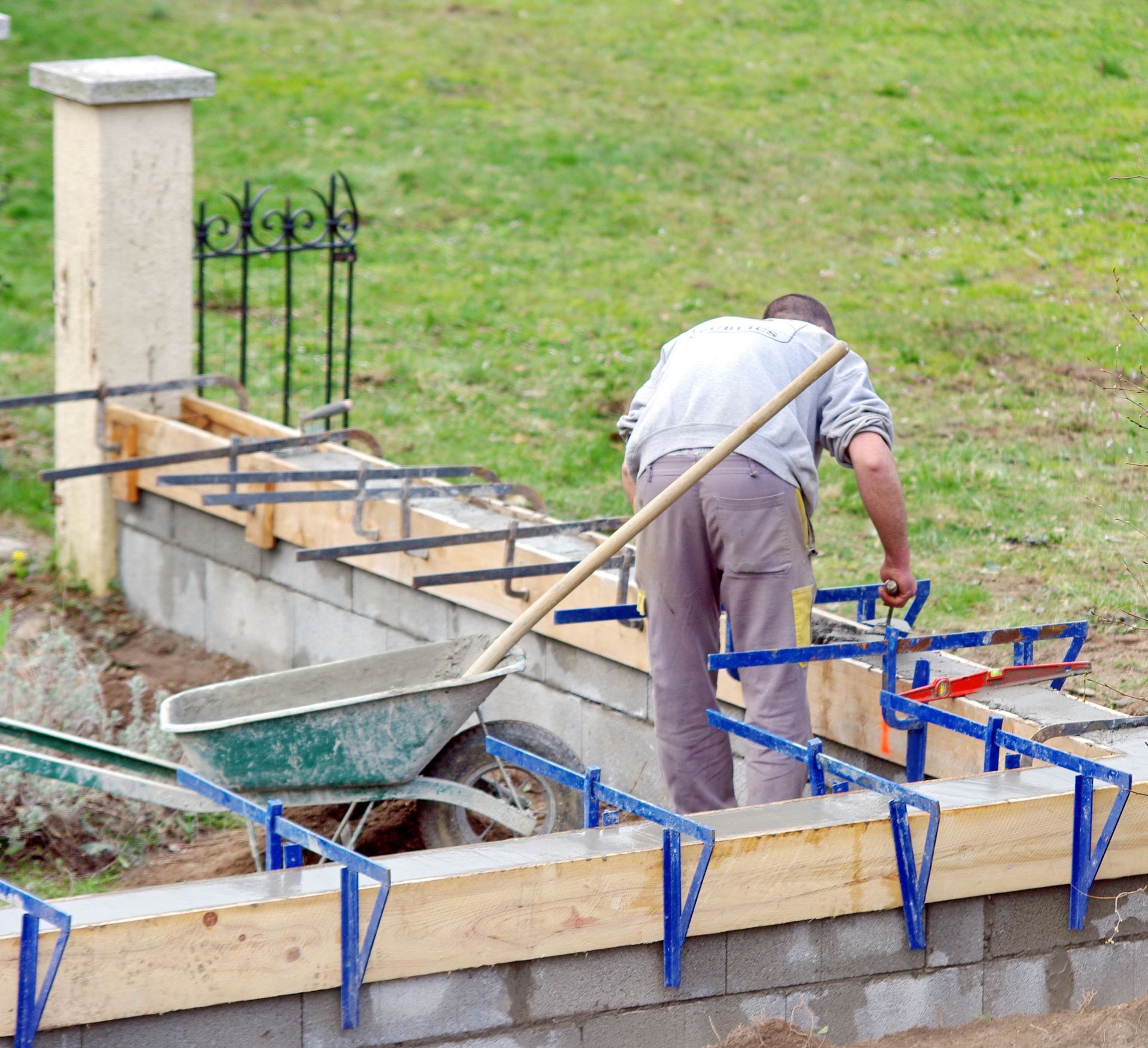 Un homme construit une structure en béton à l'extérieur à l'aide d'une brouette et d'outils.