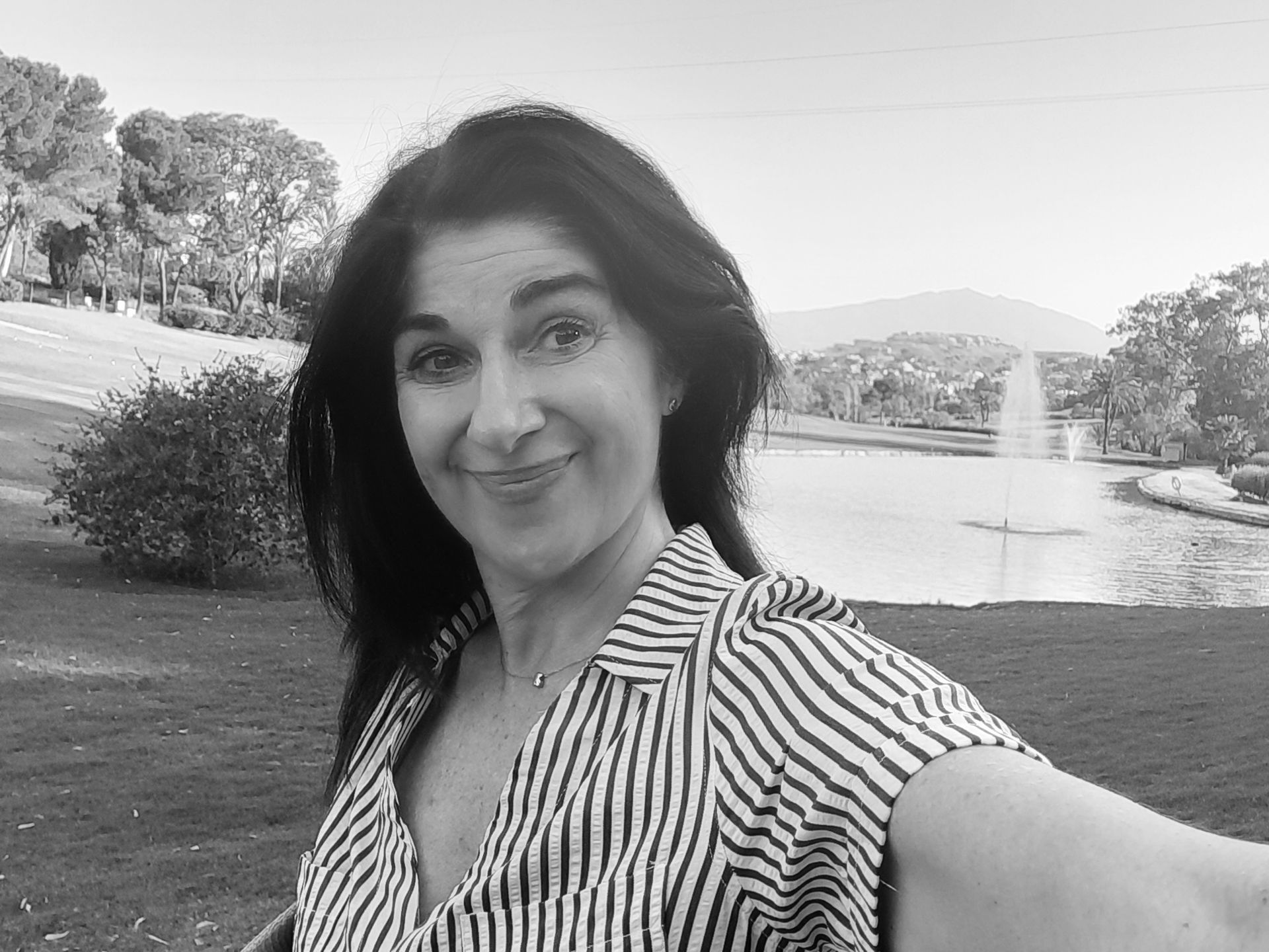 Una persona con una camisa de rayas sonríe mientras se toma una selfie al aire libre